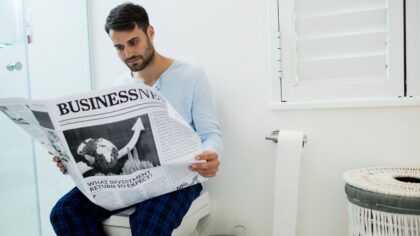 mężczyzna czyta gazetę siedząc na toalecie